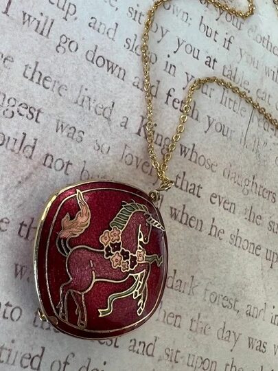 A close up of a vintage horse pendant necklace with a hors.