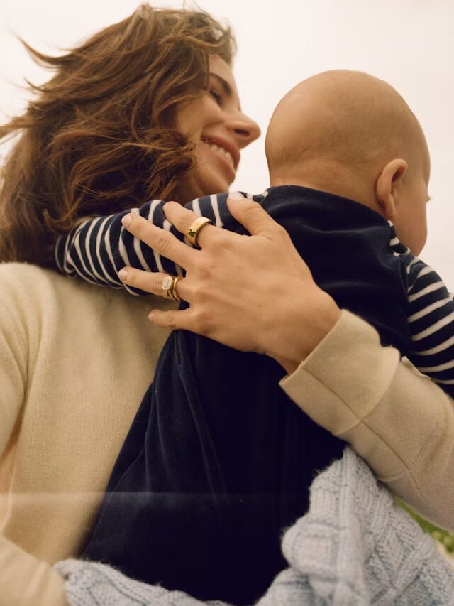 A mother holding a baby, wearing the Oura Ring. 