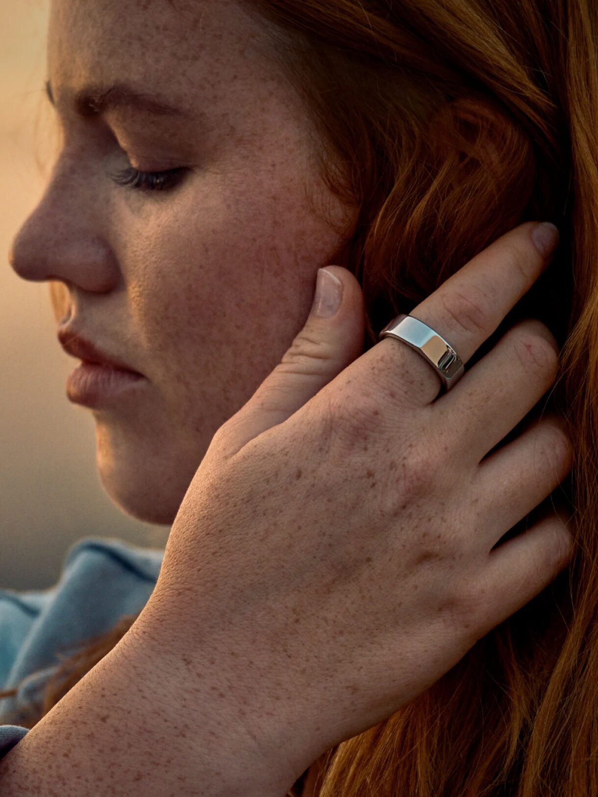 A model sweeping their hand by their ear, wearing an Oura ring. 