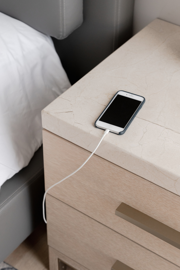 iPhone charging on a bedside table, shot from above, next to a clean bed