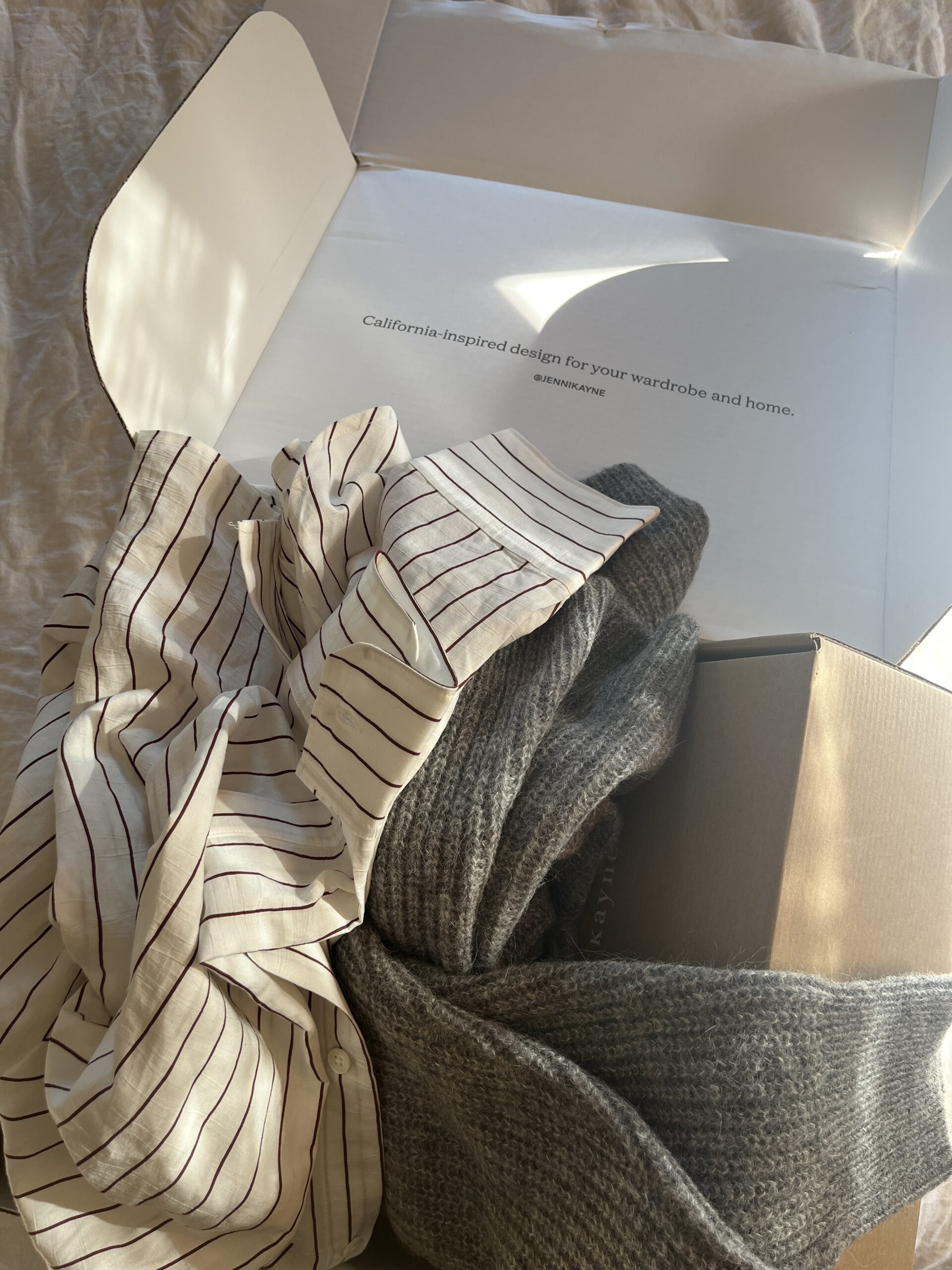 An open box with a striped shirt and gray sweater lying in it.