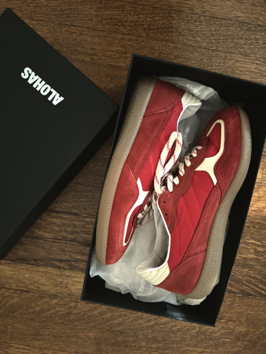 Red and white sneakers in a black shoebox on a wooden surface.