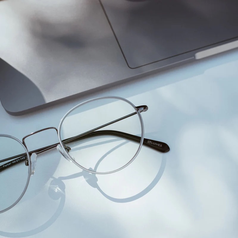 Round eyeglasses resting on a light blue surface beside a partially visible laptop.