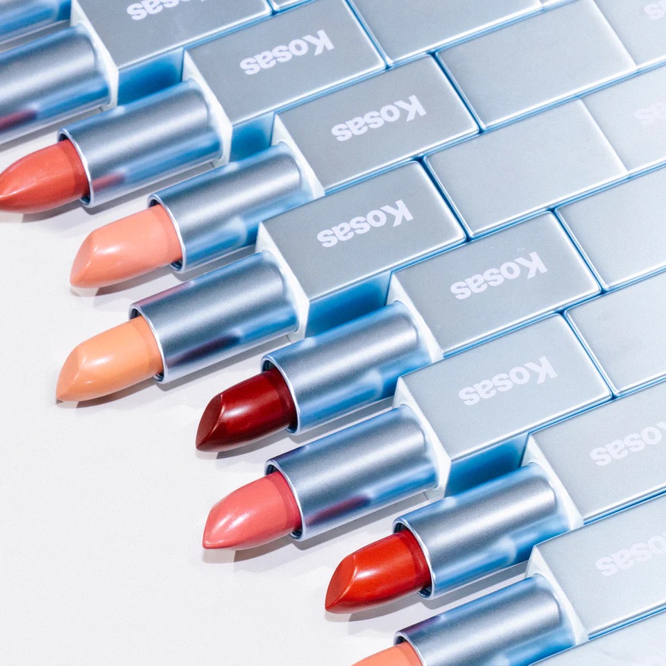 A row of open lipstick tubes with silver cases and various shades, arranged in a diagonal line on a light surface.