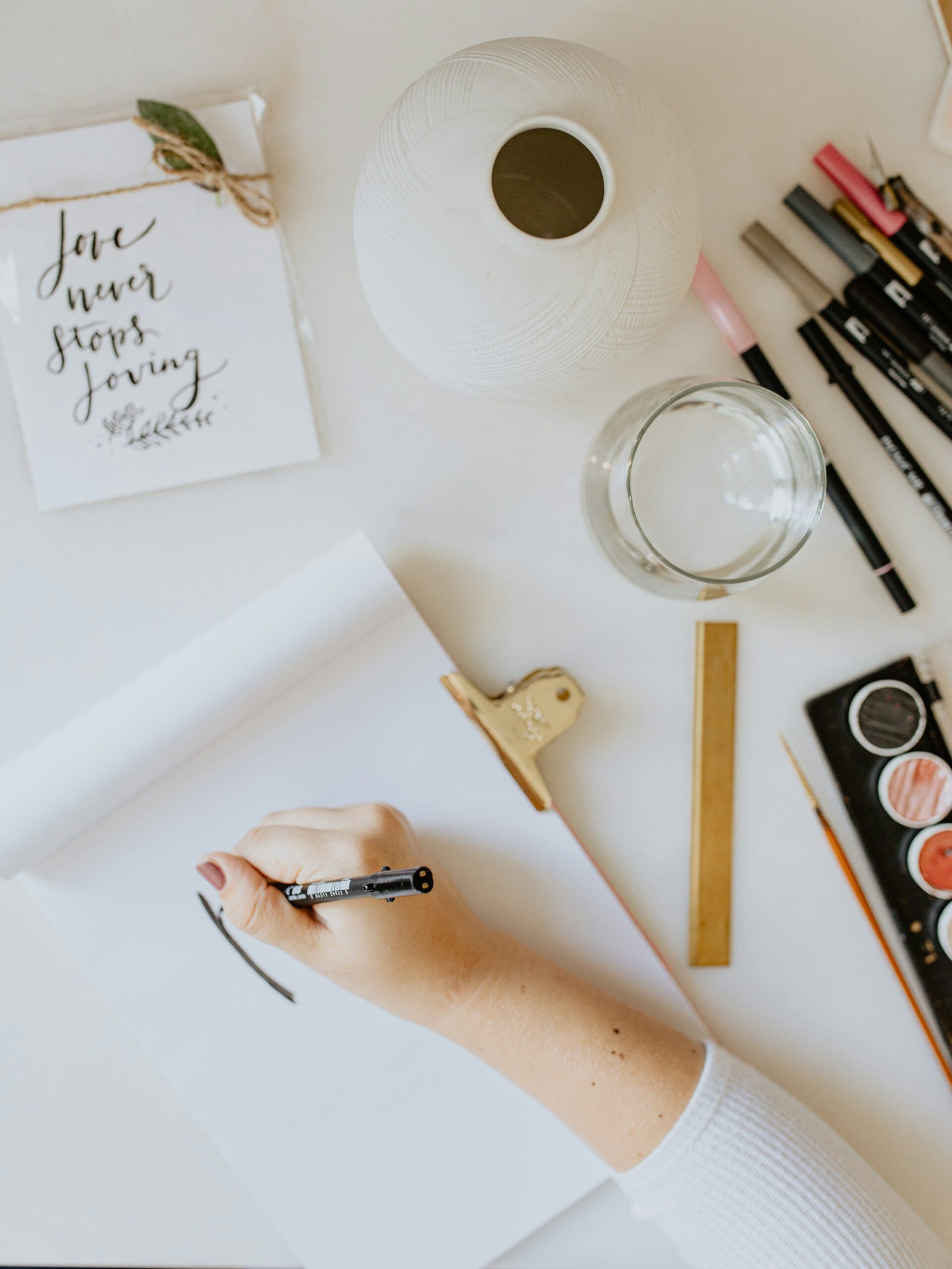 Close up of a hand creating a design on a blank piece of paper, while surrounded by arts and crafts materials.