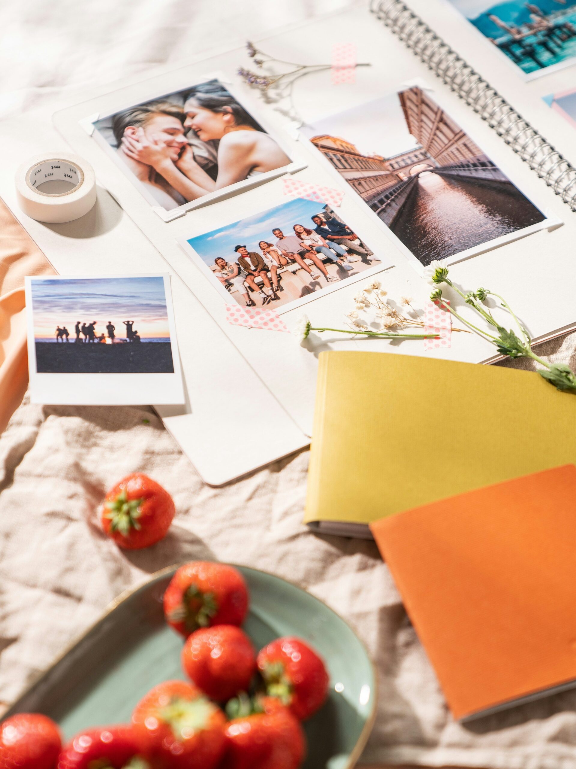 An open notebook filled with polaroid photos, and surrounded by craft materials and a plate of strawberries. 