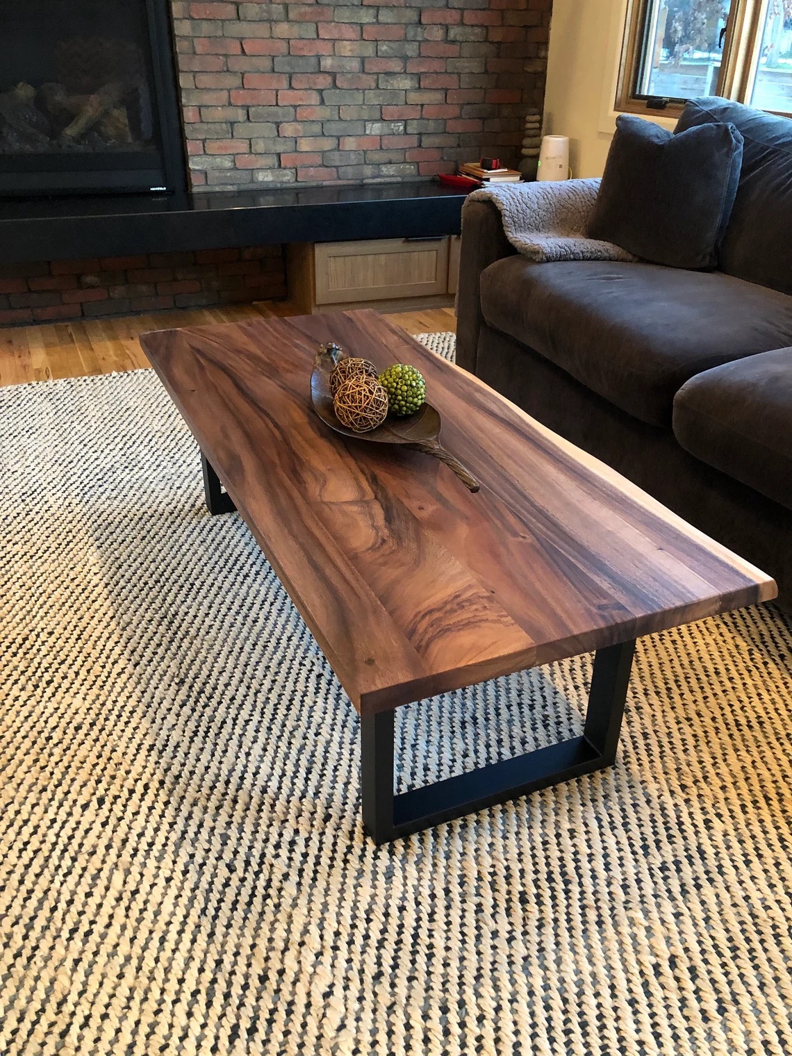 Rustic wooden coffee table on a patterned rug, with decorative items on top, next to a brown sofa. Brick fireplace in the background.