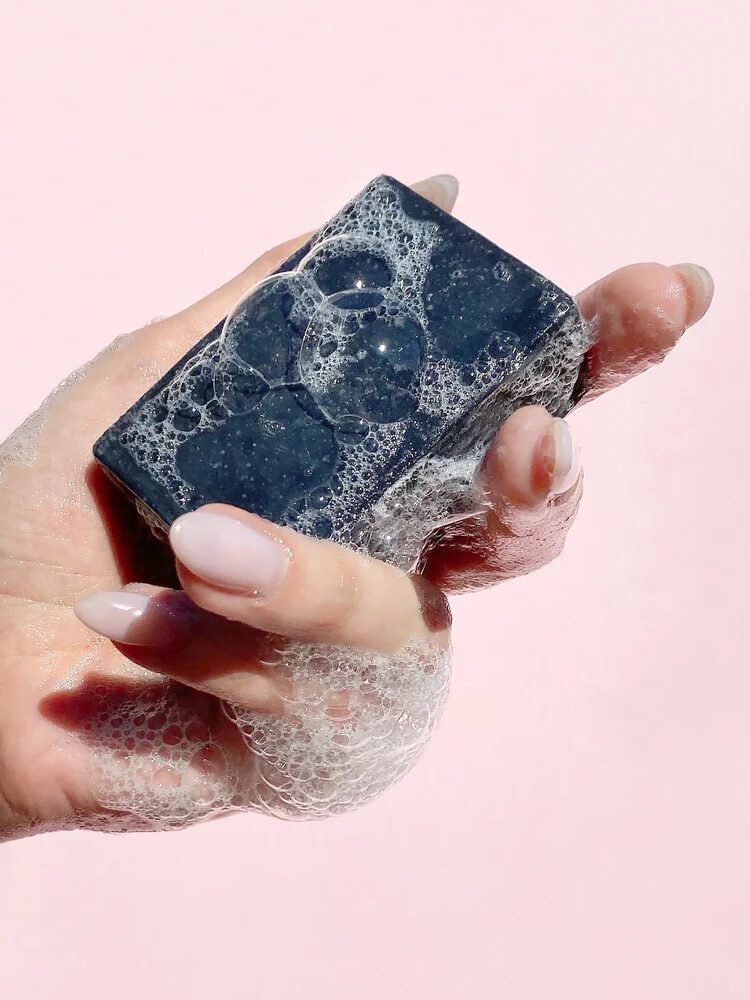 A hand holding a sudsy Herbivore Botanicals soap. 