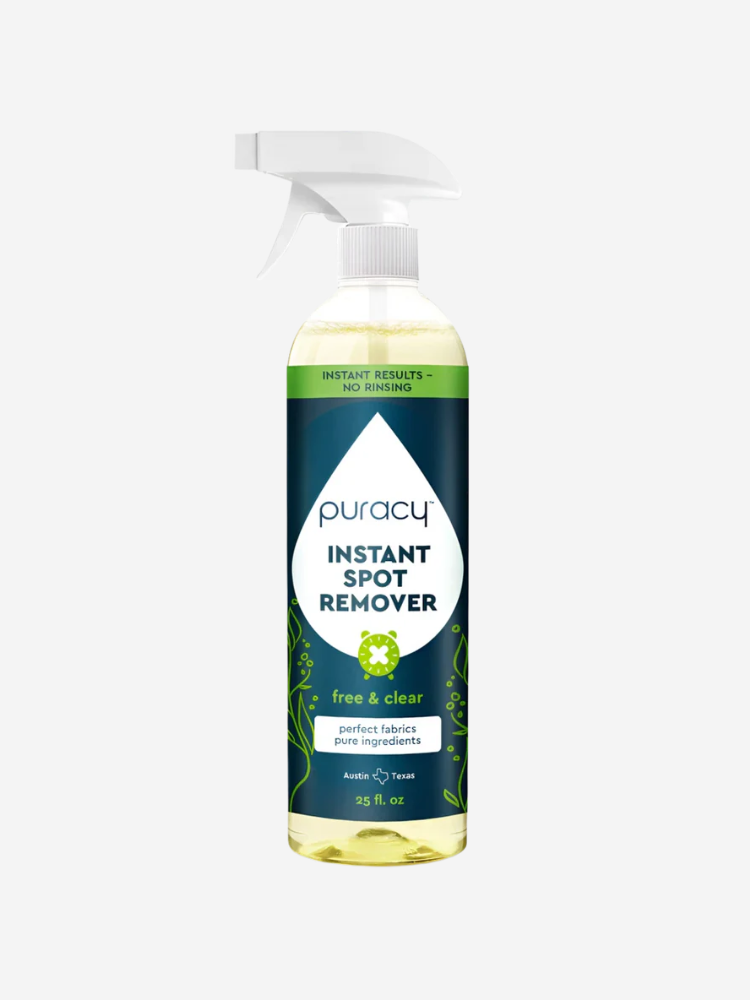 A bottle of Puracy Instant Spot Remover, 25 fl oz, with a spray nozzle. The label is blue and white, featuring green plant graphics and text about its formula and origin.