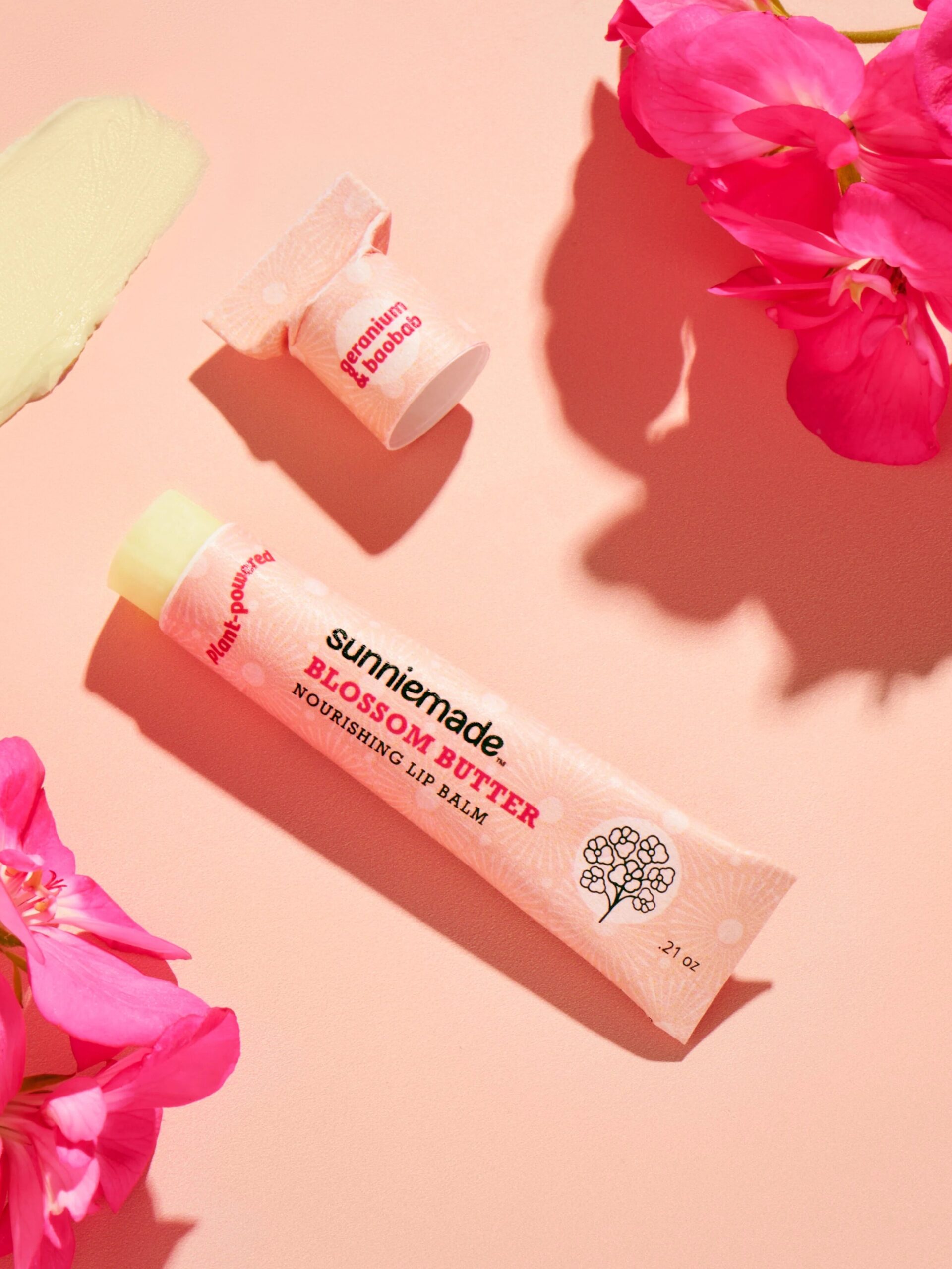 A Sunniemade lip balm surrounded by pink flowers. 