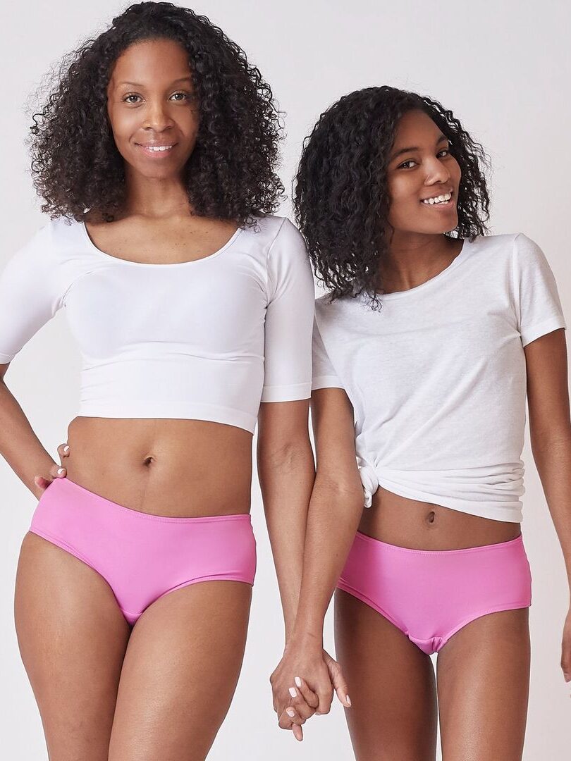 A mother and daughter hold hands, while both wear pink Ruby Love period underwear. 