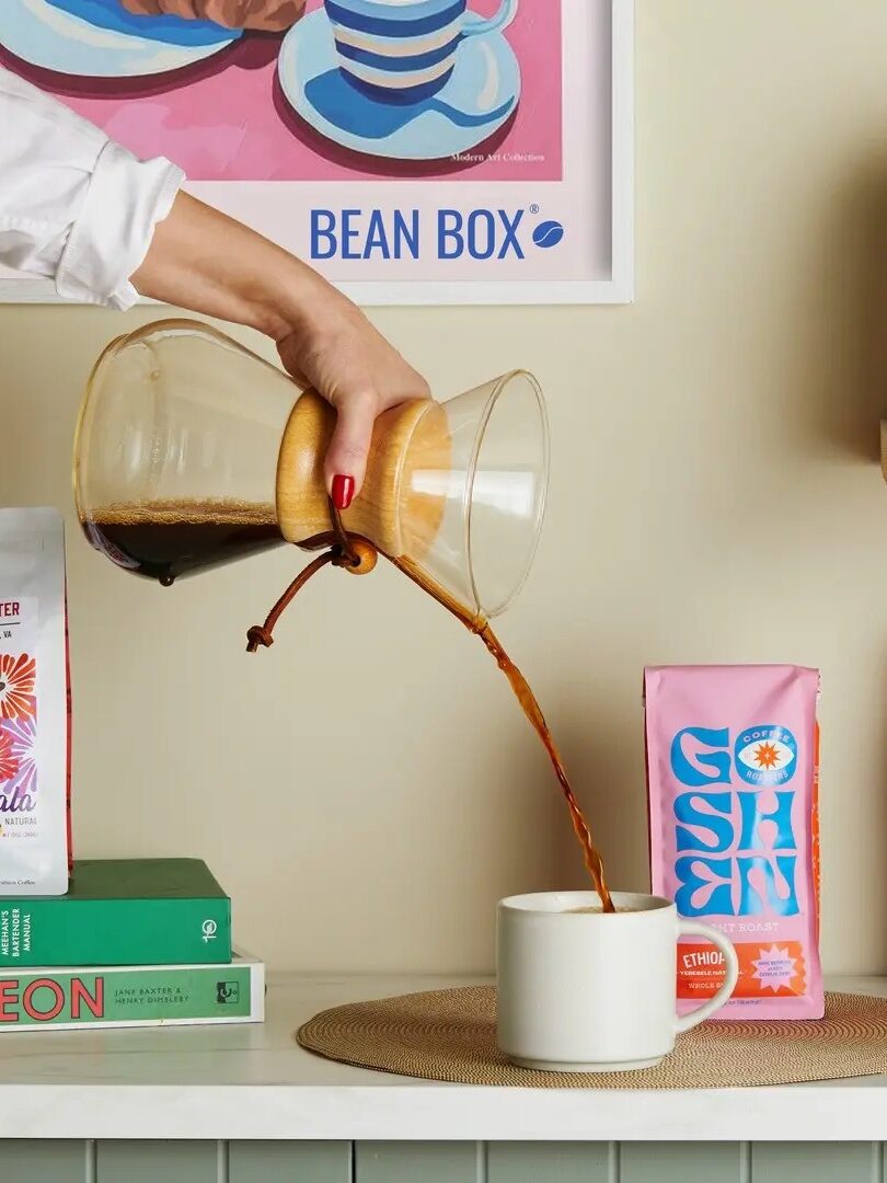 Close up of pour-over coffee, being poured into a mug with Bean Box coffee bags behind it. 