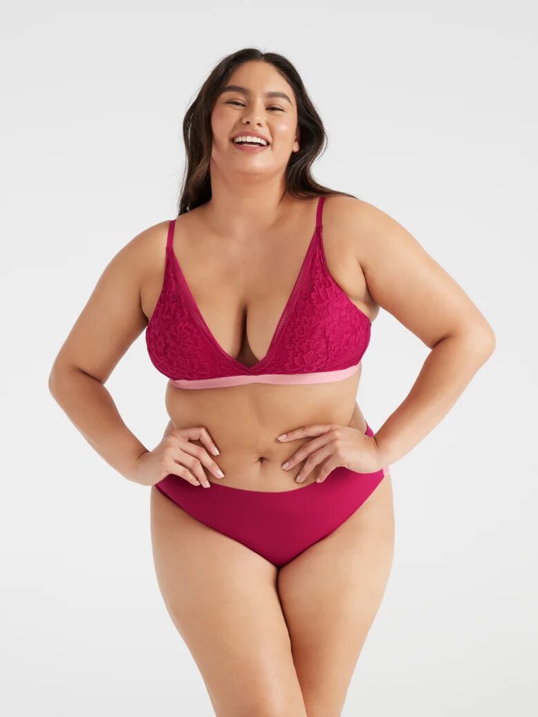 A plus size model wearing a bright fuchsia lace v-neck bra and seamless panty set from Knix. 