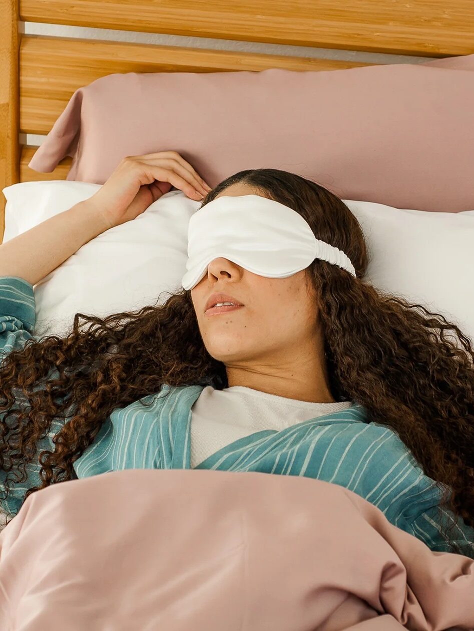 A model in bed wearing a Nest Bedding sleep mask. 