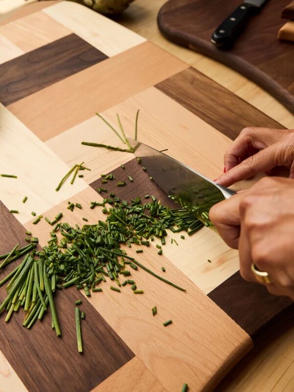 A pair of hands chopping chives on an Avocado cutting board.