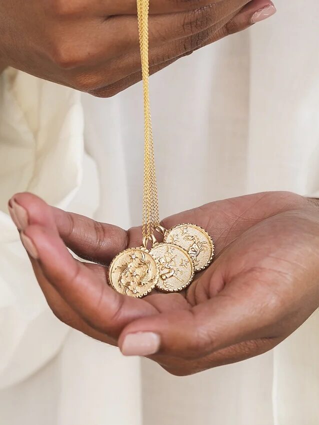 Close up of a hold holding three Brilliant Earth Zodiac pendants. 