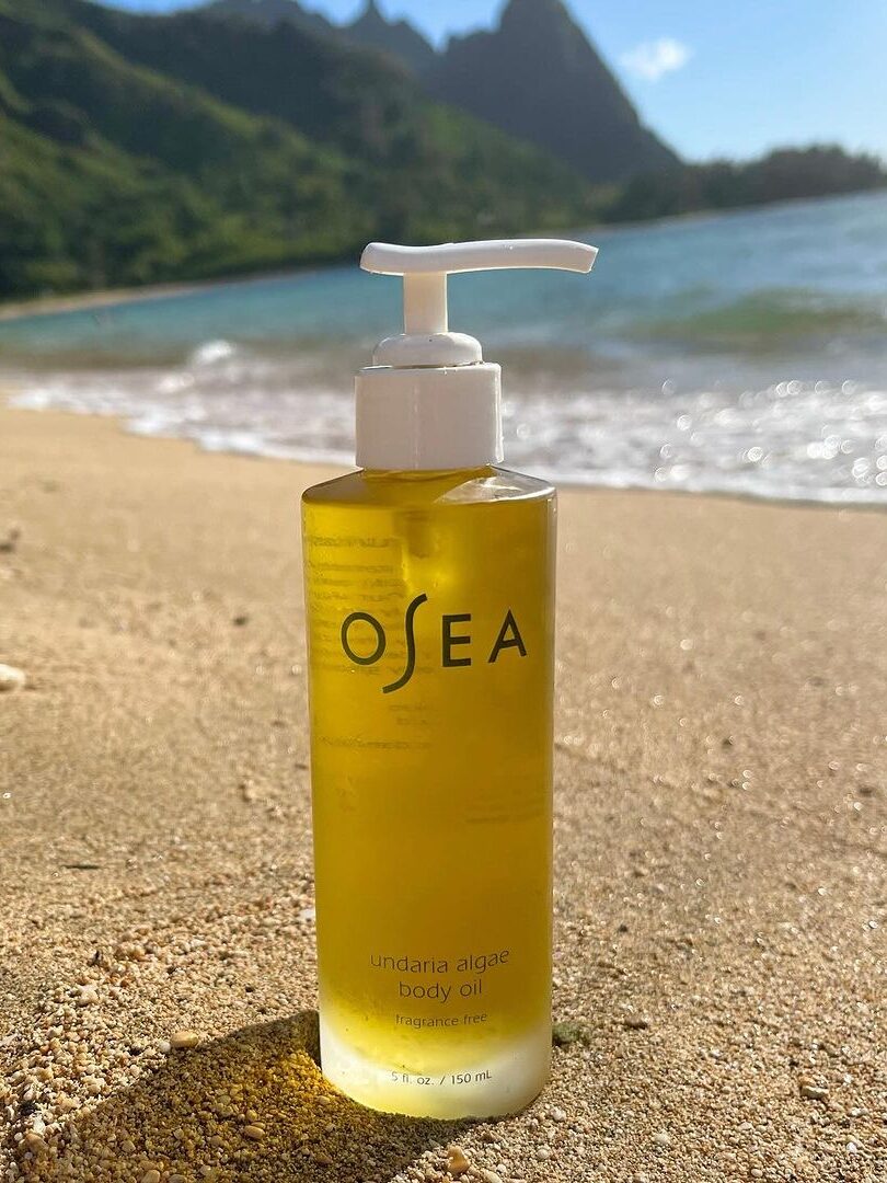 An OSEA body oil set on beach sand. 