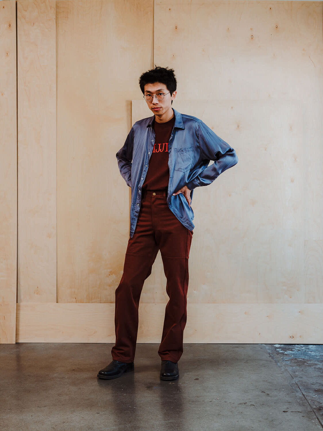 A model wearing a long sleeve denim shirt with a burgundy tee and pants from IJJI. 