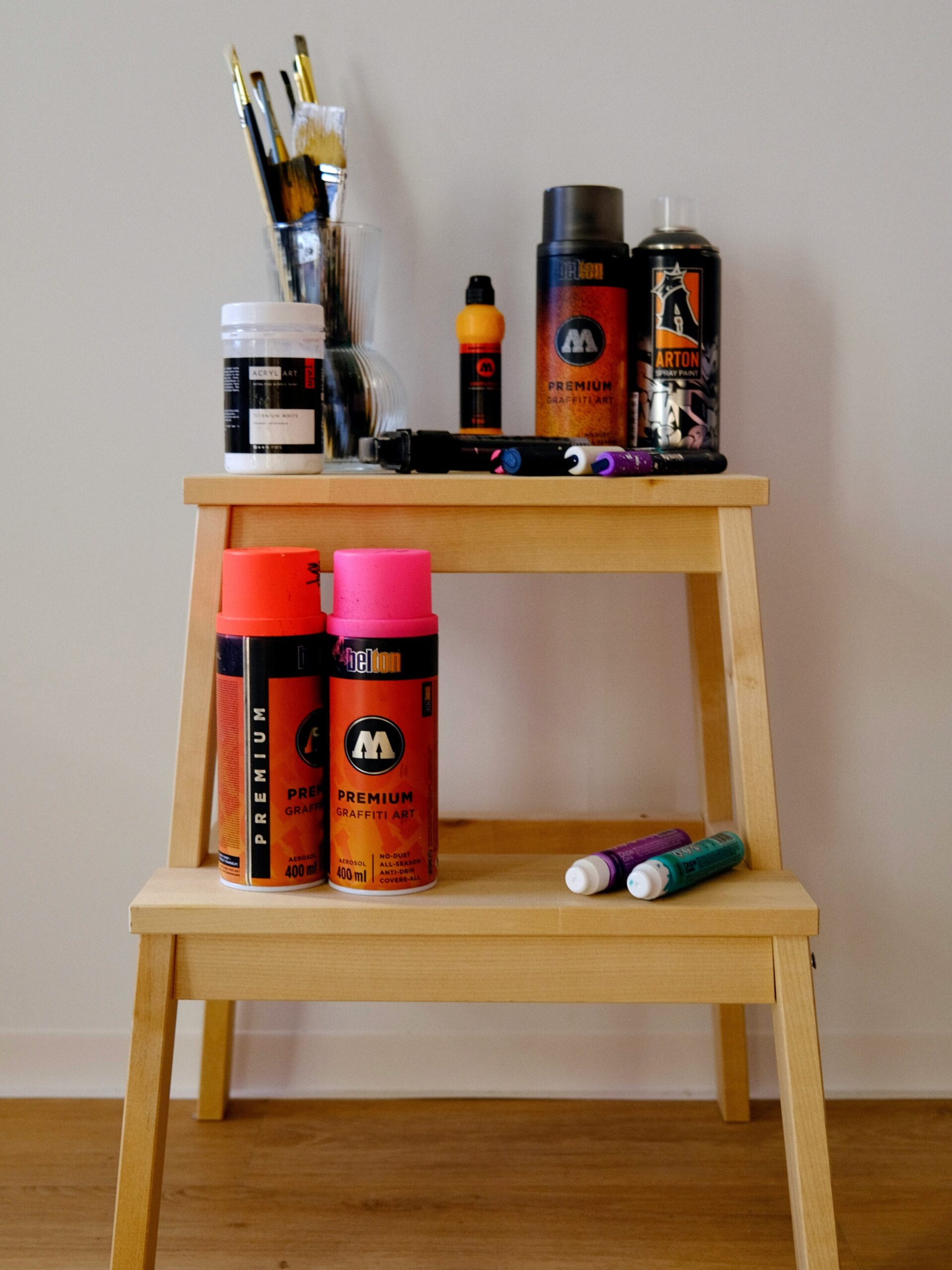 A variety of arts and crafts materials displayed on a two tier wooden stepping stool. 