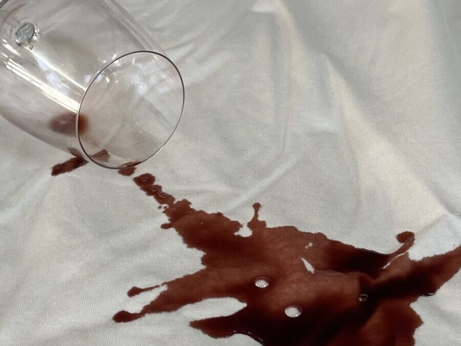 A tipped-over wine glass with red wine creating a vivid stain on the smooth surface of an organic mattress.