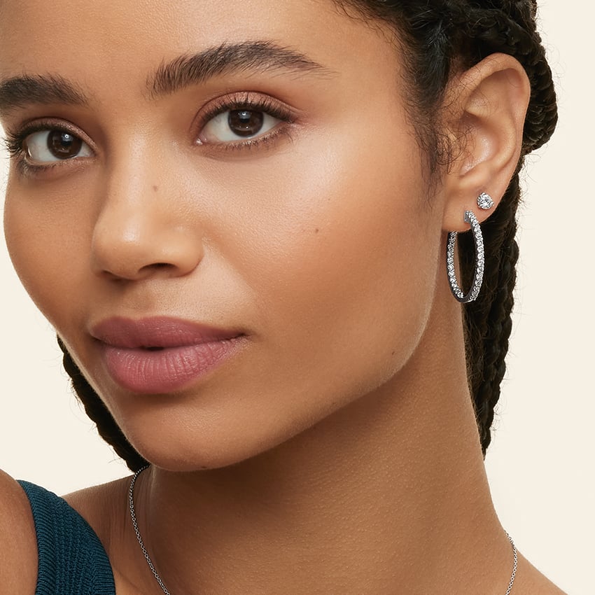 A woman with braided hair wears hoop earrings and a blue top, looking directly ahead against a plain background.