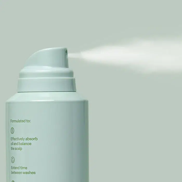 A spray can releasing mist against a light green background, with text on the can detailing its benefits for scalp care.