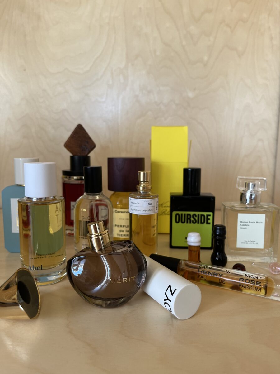 A collection of various perfume bottles and samples arranged on a light wooden surface.