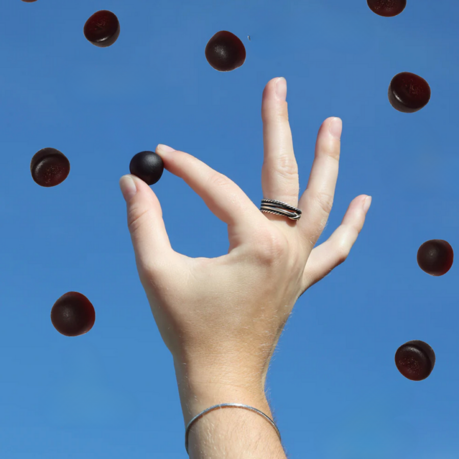 A hand with rings holds a small black sphere against a clear blue sky, surrounded by similar floating spheres.