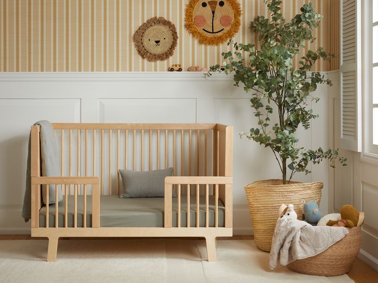 A nursery with a wooden crib, a large potted plant, and a basket of toys. Animal wall decor hangs above, and sunlight streams through a window on the right.