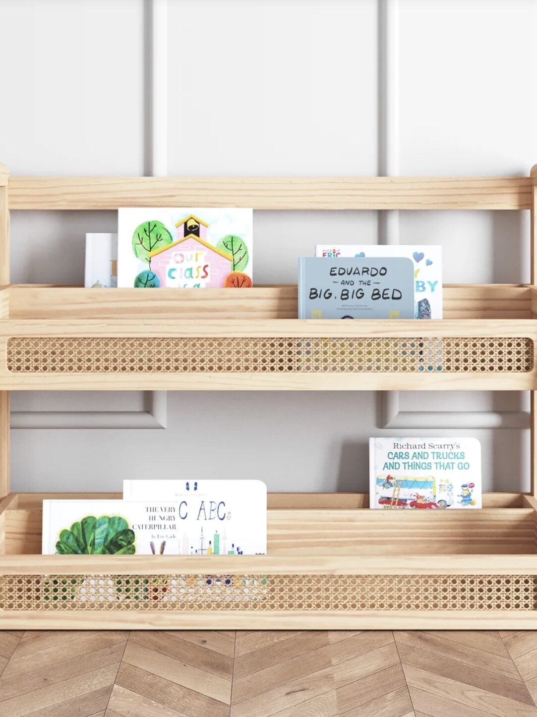 A wooden two-tier bookshelf holds children's books, featuring colorful covers with illustrations, on a parquet floor.