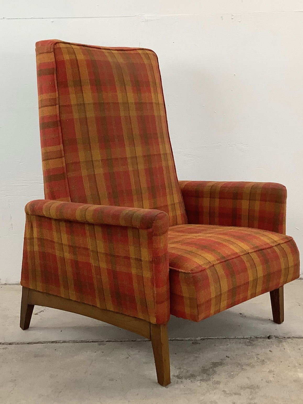 A vintage armchair with red and orange plaid upholstery on a wooden base, set against a plain white wall.