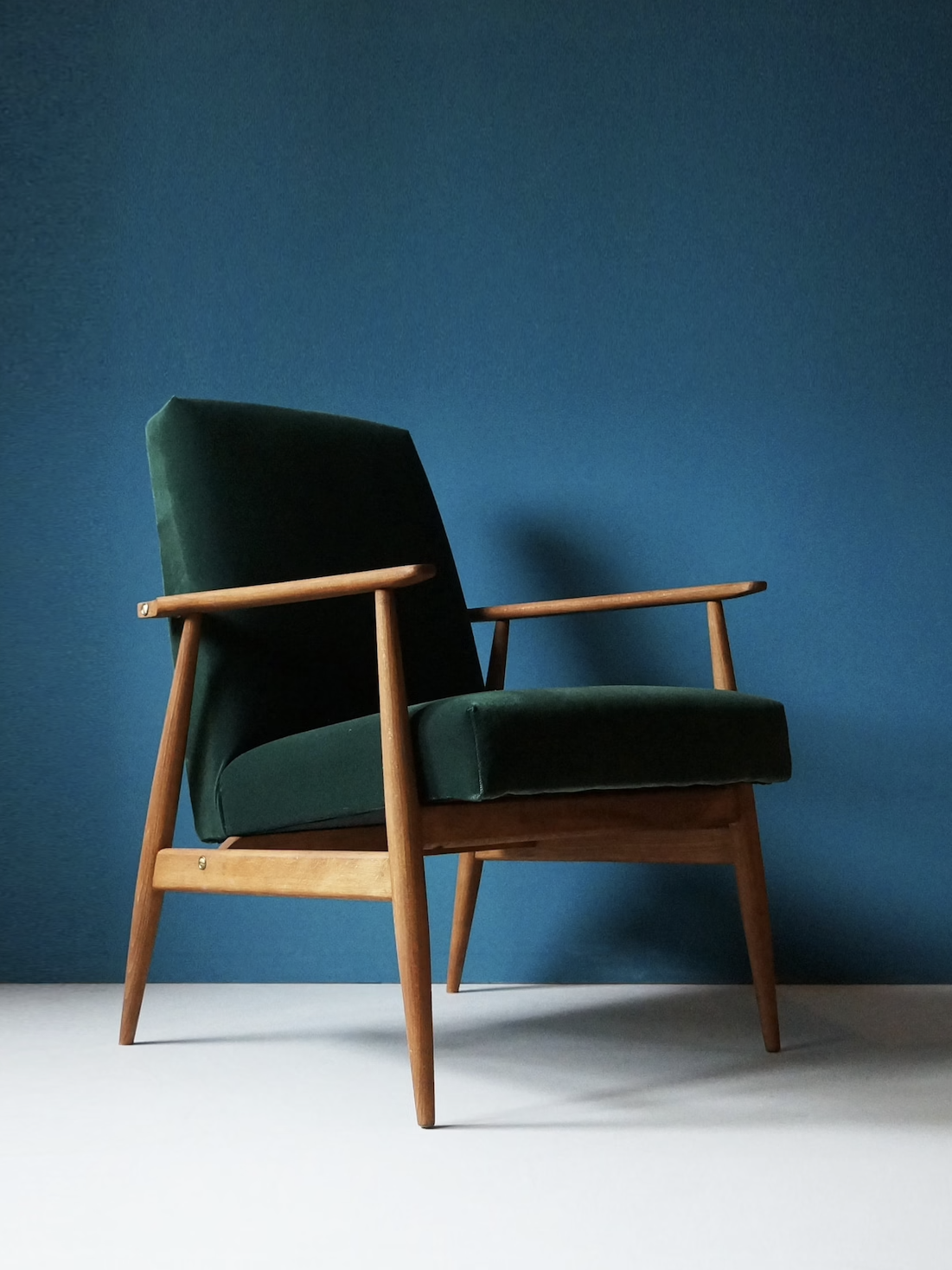 A wooden armchair with green upholstery on a light floor against a blue wall.