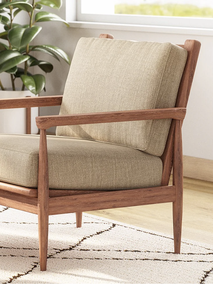 A mid-century modern armchair with beige cushions and a wooden frame is placed on a patterned rug, next to a potted plant by a sunlit window.