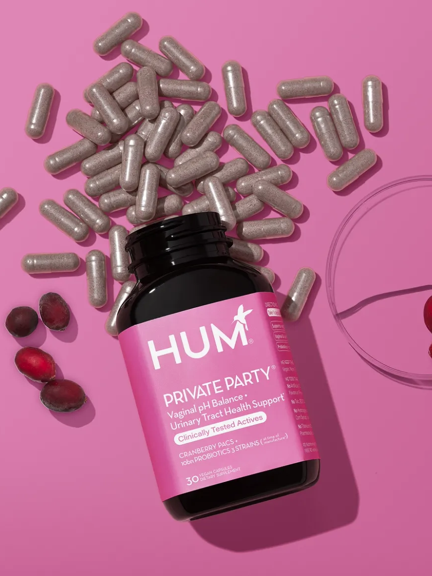 A bottle labeled "HUM Private Party," surrounded by capsules and a dish with cranberries, on a pink background.