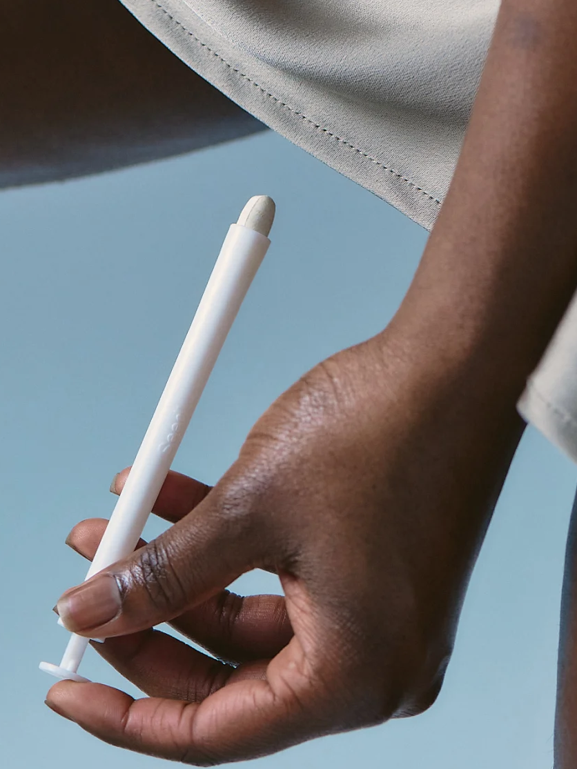 Person holding a white tampon applicator near their leg against a light blue background.