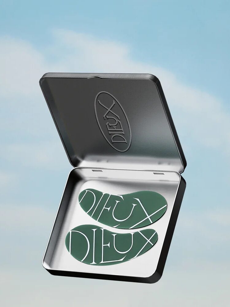 A silver case opened to reveal green under-eye patches with "DIEUX" printed on them, set against a blue sky background.