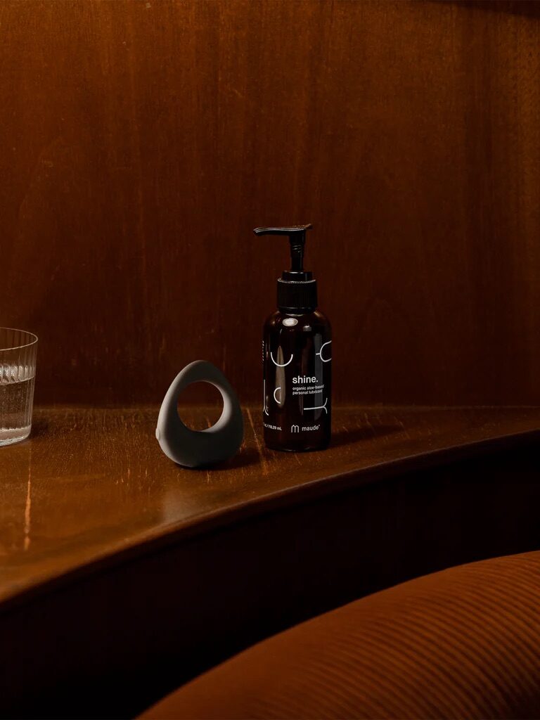 A bottle of hand wash, a small ceramic object, and a glass sit on a wooden shelf.