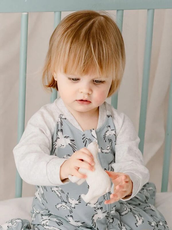 A toddler in a patterned outfit sits on a blue chair, looking at a white object in their hands.