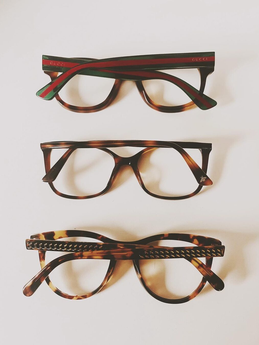 Three pairs of eyeglass frames: top pair with green and red stripes, middle and bottom pairs with tortoiseshell patterns.