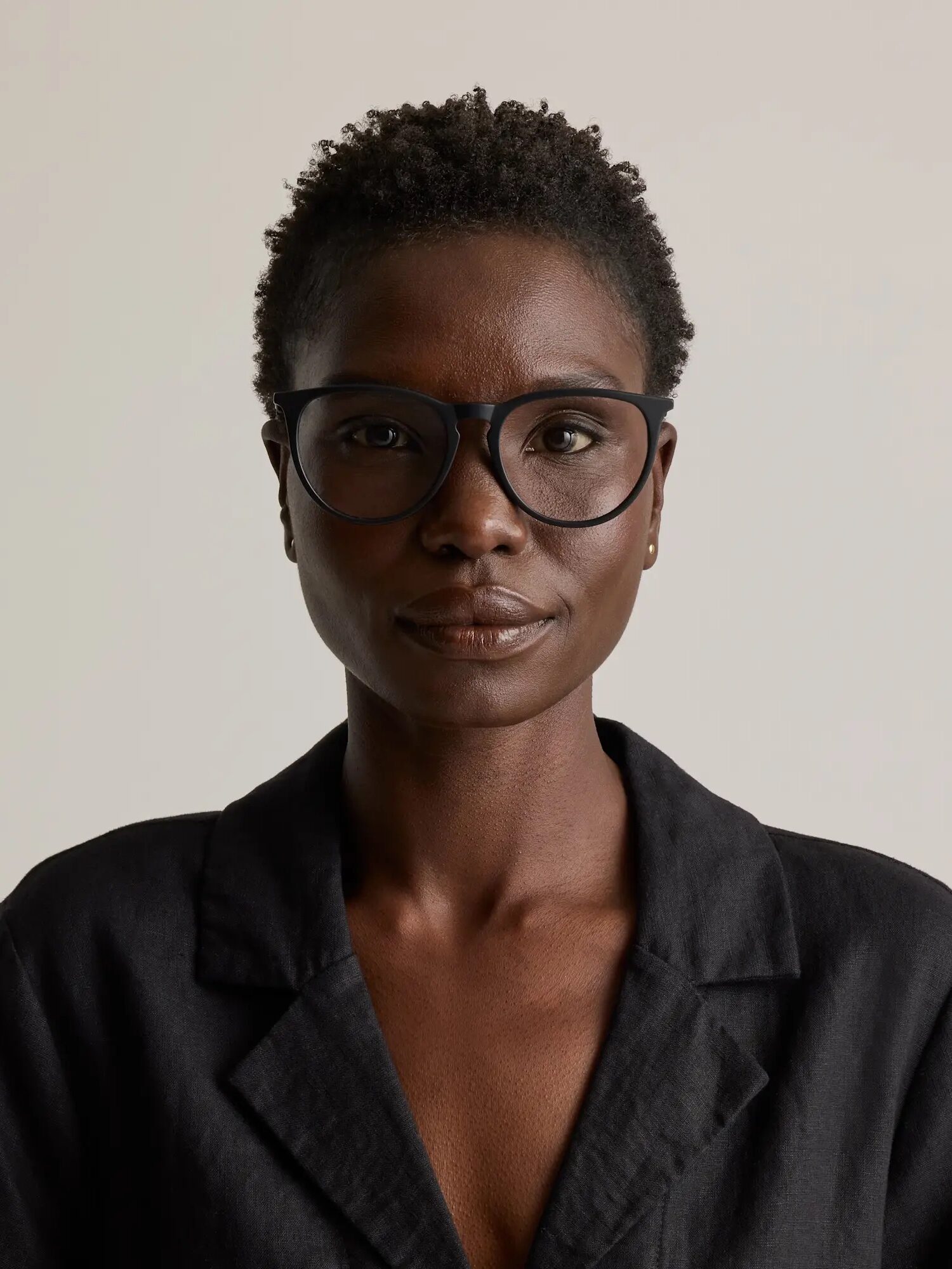 A person wearing black-framed glasses and a black jacket stares directly at the camera against a plain background.