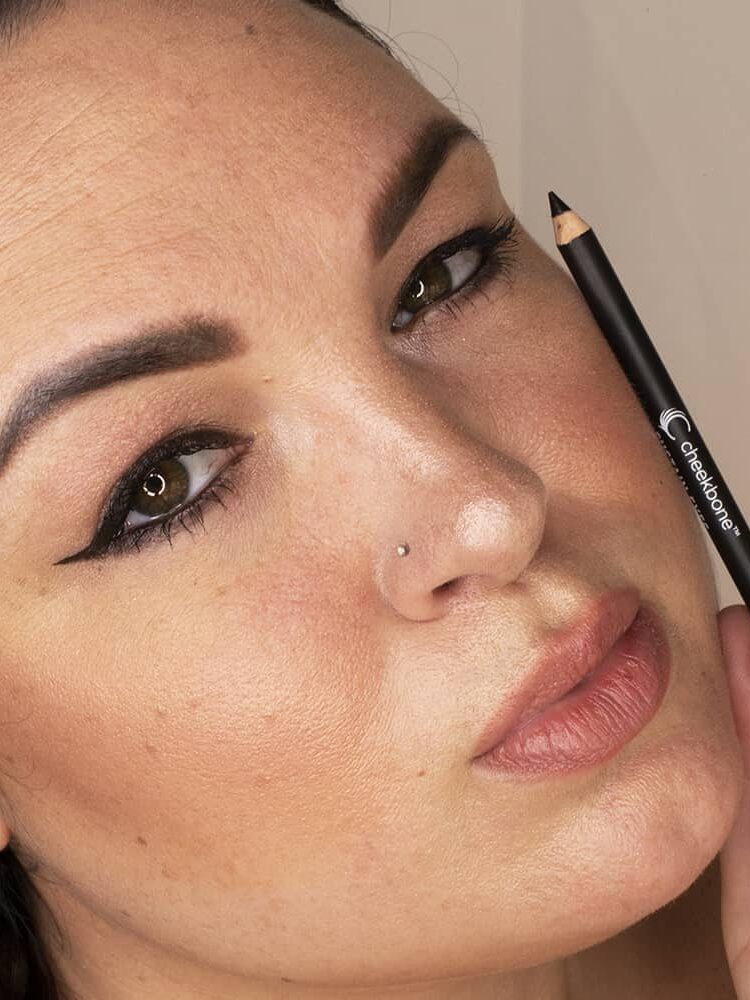 Close-up of a person holding a black eyeliner pencil near their face, with bold eyeliner makeup applied.