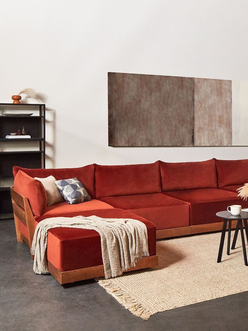 A living room with a red sectional sofa, a beige rug, a round coffee table, and wall art. Shelving, a floor lamp, and curtains complete the modern decor.