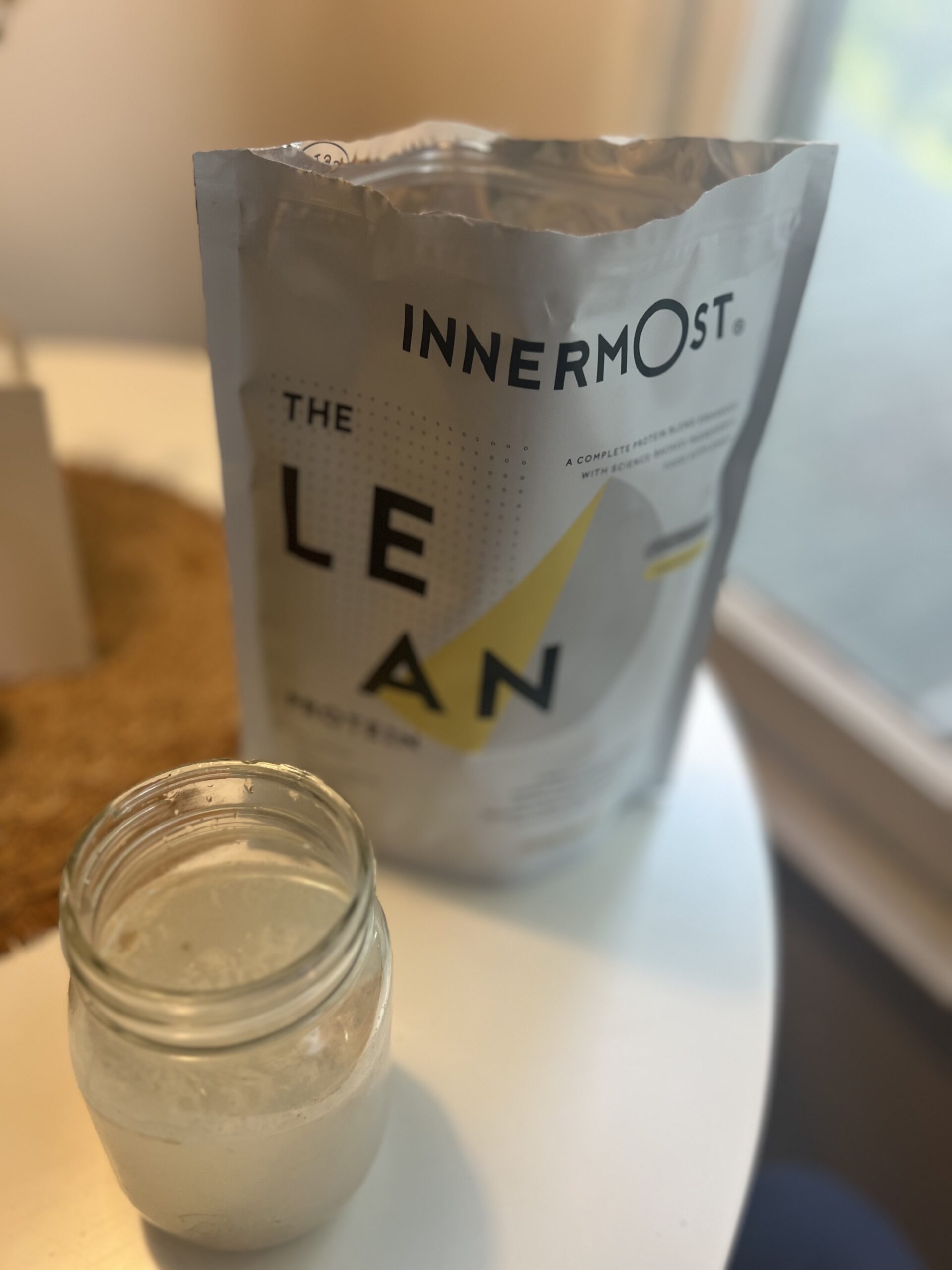 A jar filled with a smoothie sits on a table next to a bag of Innermost "The Lean" protein powder.