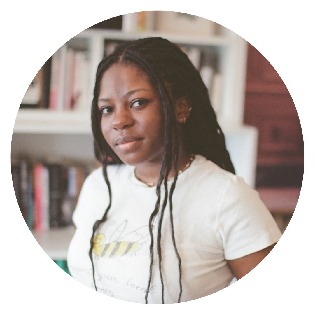 Langa Chinyoka has long braided hair, wears a white T-shirt and stands in front of a bookshelf.