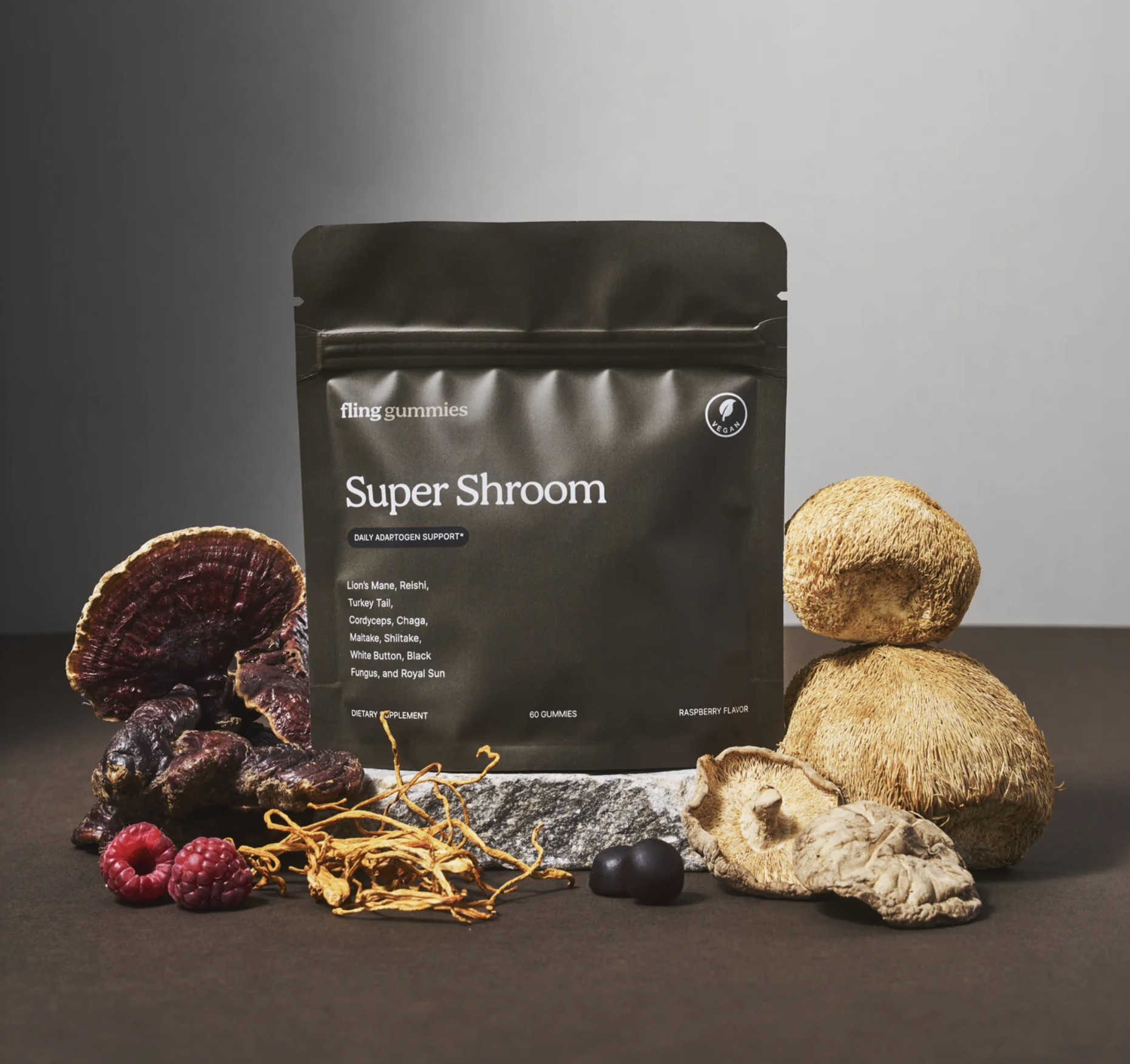 Bag of "Super Shroom" gummies surrounded by various mushrooms and berries on a gray surface.