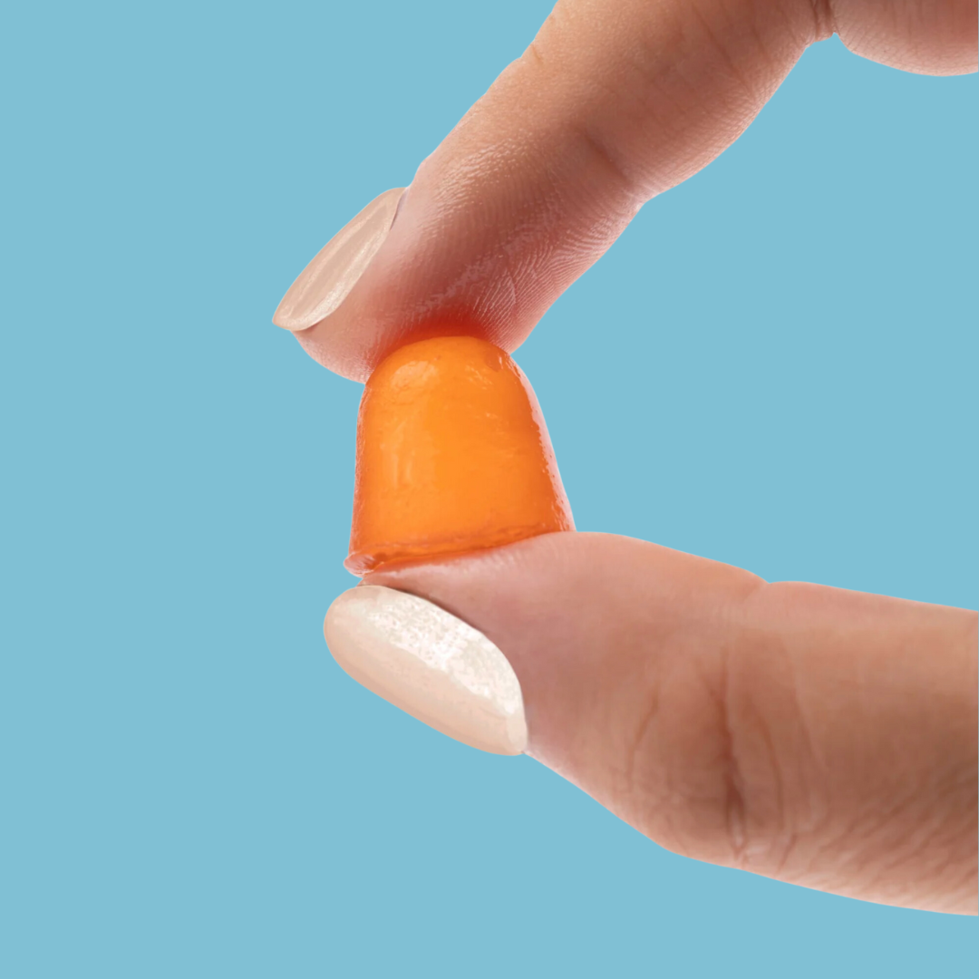 A hand holds an orange candy between two fingers against a light blue background.