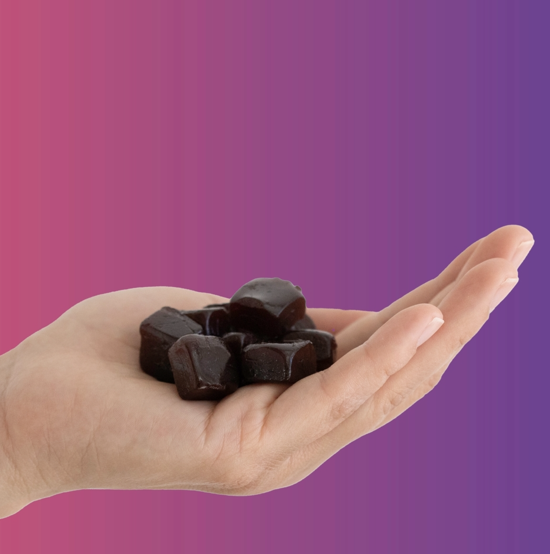 A hand holding several small, dark-colored gummy pieces against a gradient pink and purple background.