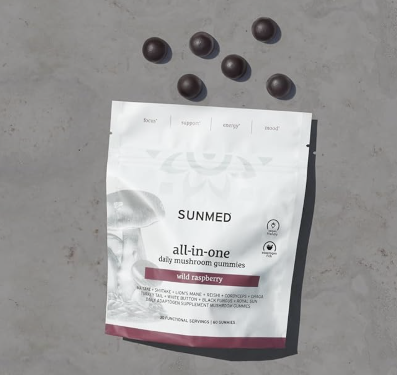 A package of Sunmed all-in-one daily mushroom gummies in wild raspberry flavor lies on a surface, surrounded by five round gummies.