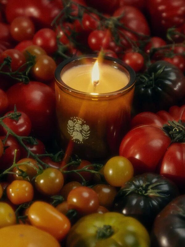 A lit candle in a glass holder is surrounded by a variety of tomatoes of different colors and sizes.