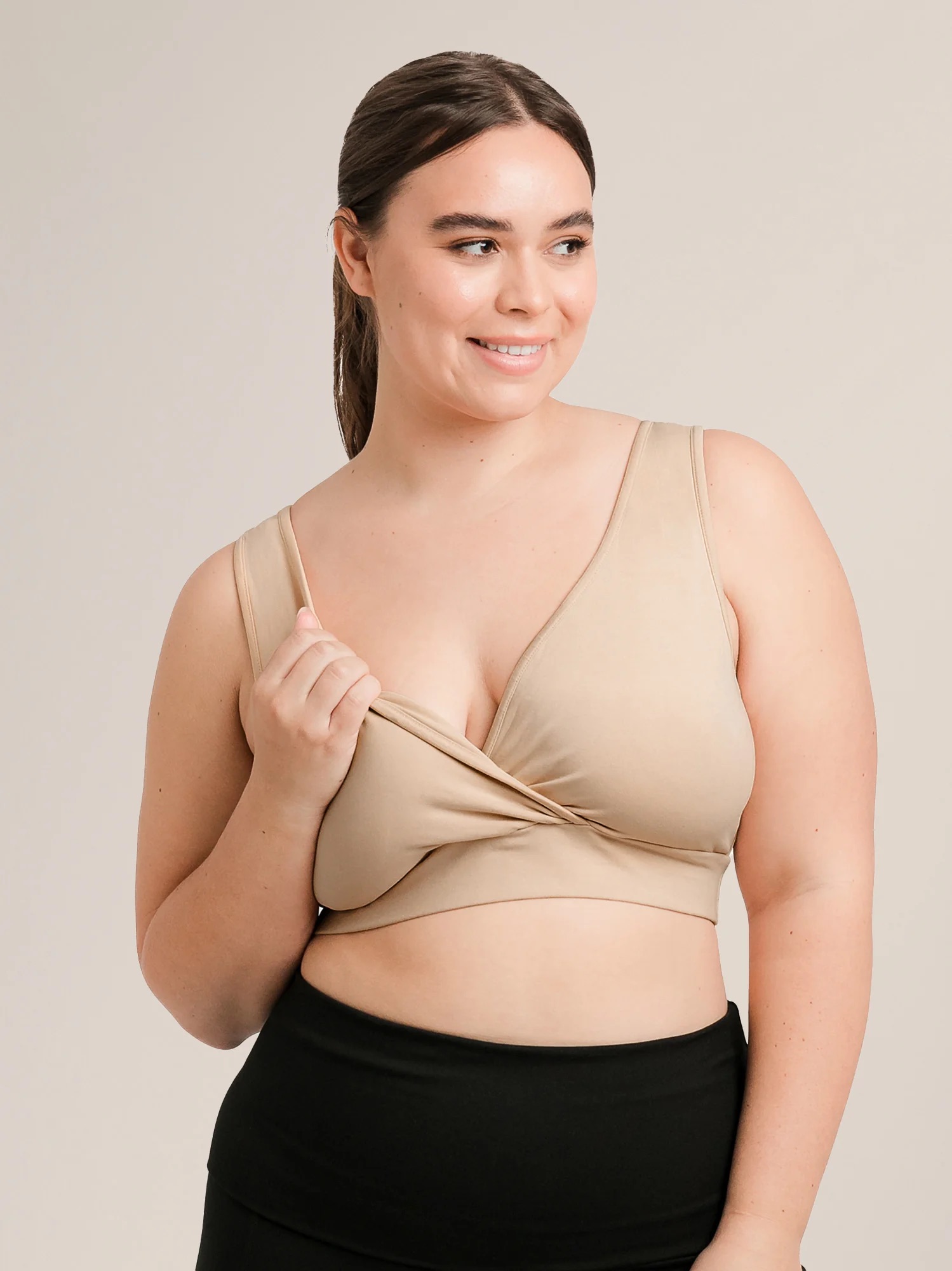 A woman in a beige wrap-style sports bra and black leggings smiles while looking to the side.